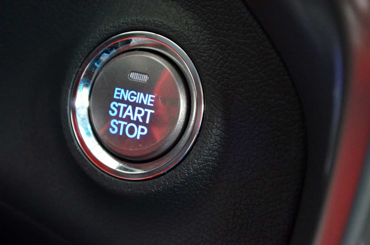 Close-up of a modern push-button car ignition with illuminated “Engine Start Stop” text inside a vehicle dashboard.