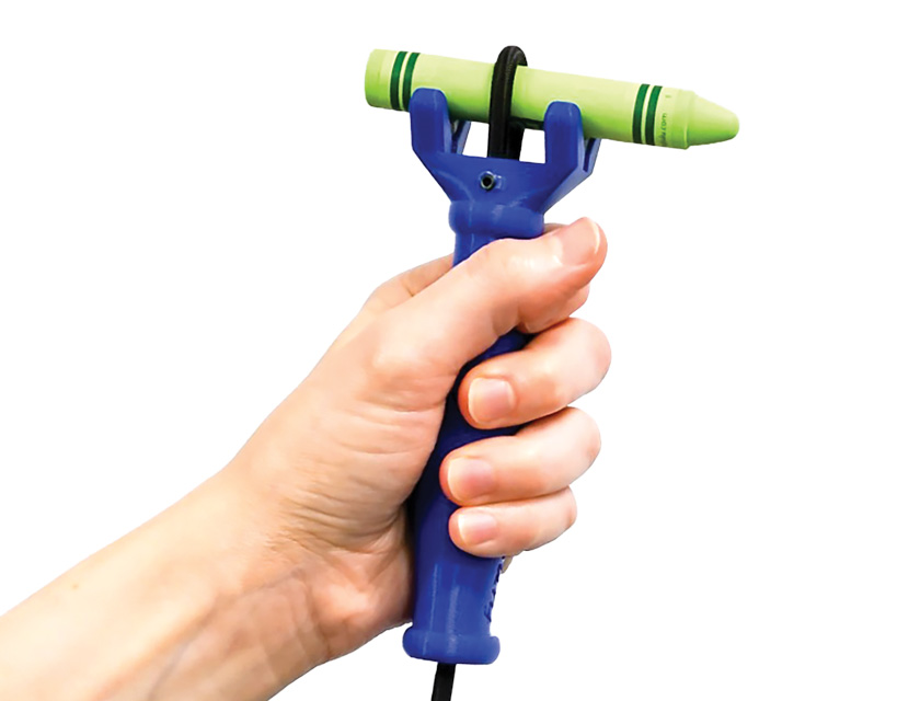 Hand holding the functionalhand assistive device with a green crayon secured horizontally.